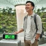 싱가포르 항공 수하물 규정 글의 대표 이미지, 싱가포르 창이 공항 쥬얼 내 인공 폭포 앞에서 수하물 무게 29.8kg이 찍힌 캐리어를 보며 환하게 웃는 아시아인 남성 여행객.