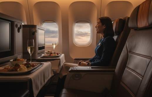 싱가포르 항공 프리미엄 이코노미 좌석에 앉아 창밖을 보며 미소 짓는 여성 승객, 기내식과 샴페인이 놓인 테이블.