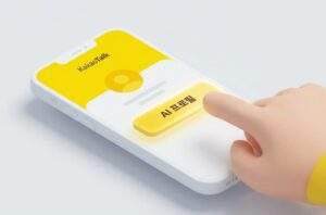 카카오 ai 프로필 만들기: 스마트폰 화면에 카카오톡 앱이 실행되어 있고, 채팅방 내의 노란색 "AI 프로필 만들기" 버튼을 사람의 손가락이 누르고 있는 3D 이미지이다. 카카오톡 로고와 전체적인 UI가 깔끔하게 표현되어 있다.