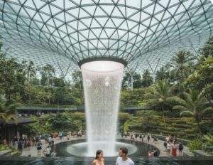 싱가포르 창이공항 쥬얼의 거대한 실내 폭포(레인 보텍스)를 배경으로 수영장에서 플로팅 조식을 즐기는 커플.