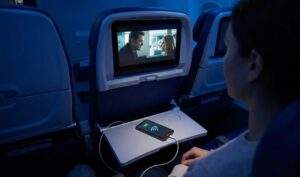 싱가포르 항공 와이파이를 이용하여 야간 비행 중 기내 엔터테인먼트 시스템으로 영화를 보며 테이블 위에서 와이파이에 연결된 스마트폰을 충전하고 있는 승객의 뒷모습.