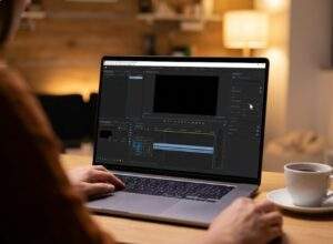 프리미어 프로 2026 AI 오디오를 편집하는 사용자의 작업 모습. 노트북 화면의 '기본 사운드' 패널에서 '음성 향상' 슬라이더를 마우스로 조절하는 장면. 편안한 재택근무 환경 배경.